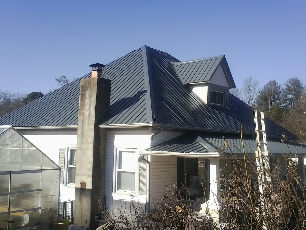 Dark blue standing seam metal roof on a white farmhouse with dormer — Slate & Tile Roof Repair by Roofing Brothers in Ooltewah