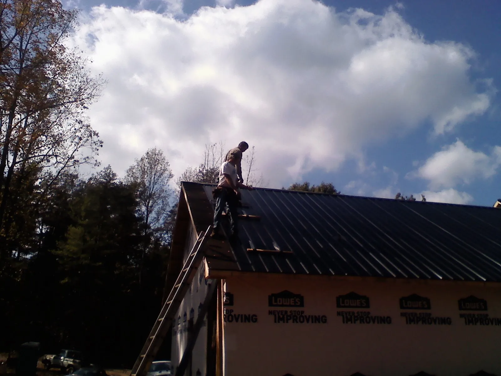 Roofer fastening dark metal panels high against a cloudy sky, from a Roof Inspection job in Ooltewah