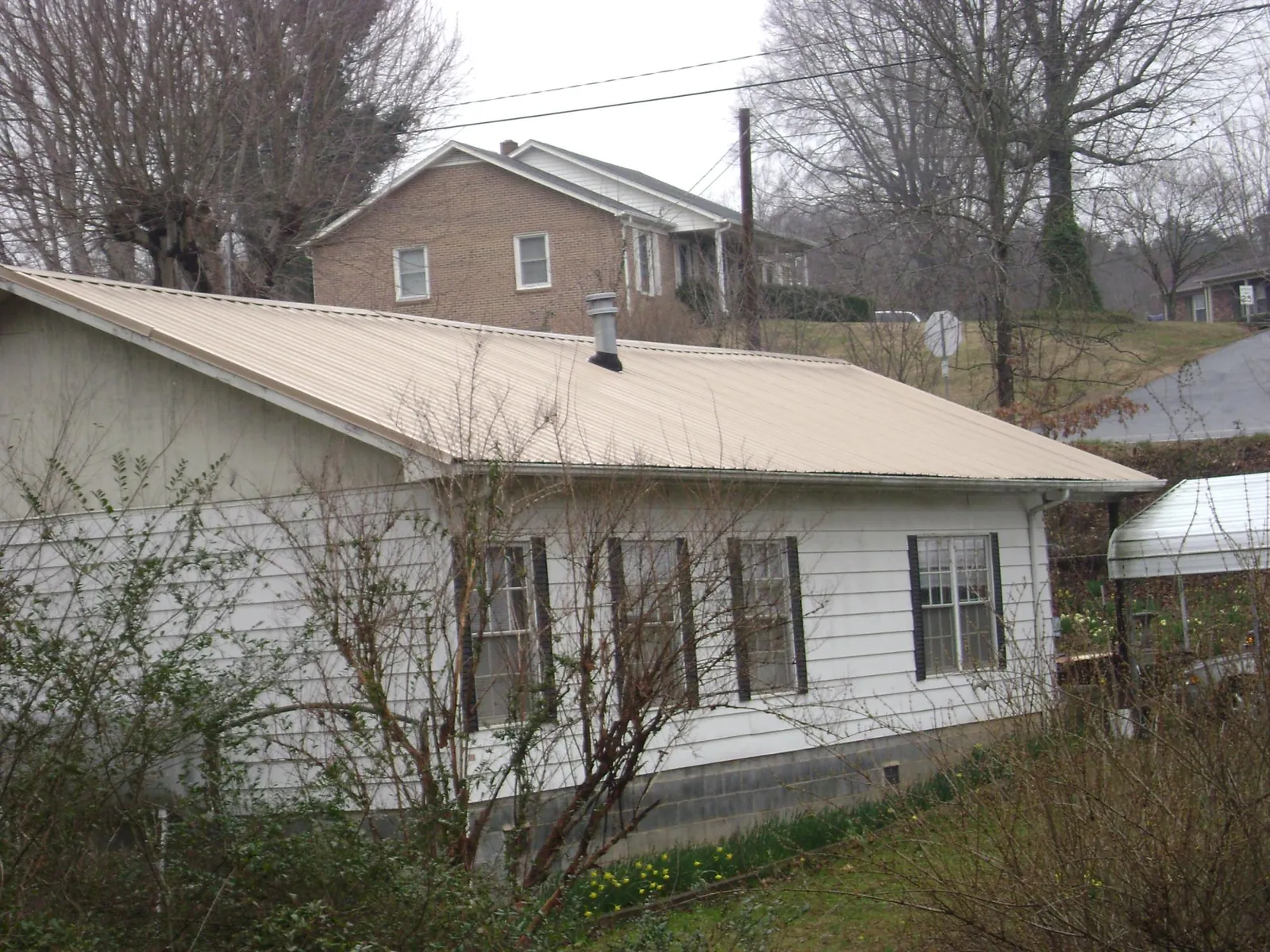 Tan metal roof on a white sided house set into a hillside — Commercial Roofing by Roofing Brothers in Ooltewah