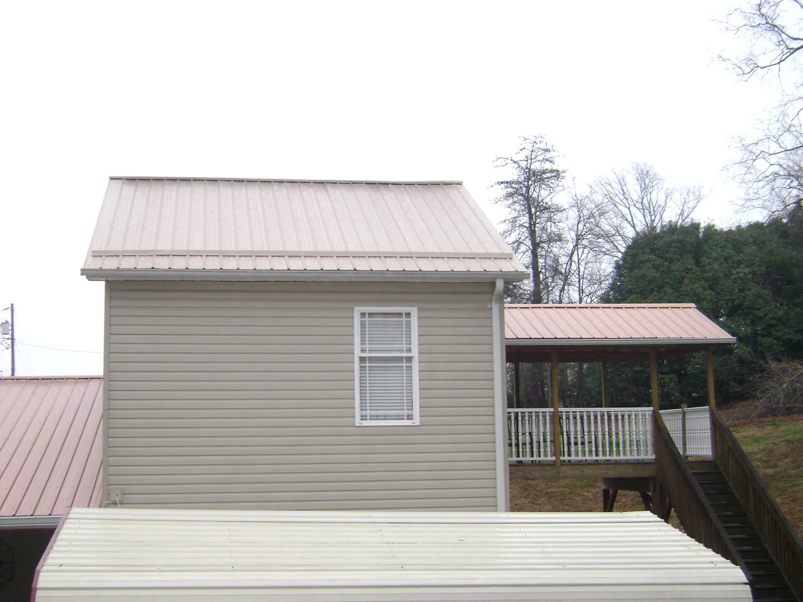 Tan metal roofs on a two story addition and attached porch, from a Roof Replacement job in Ooltewah